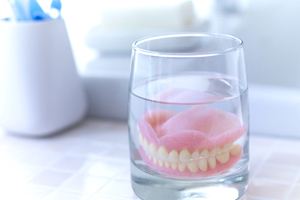 Full dentures soaking in glass on bathroom counter